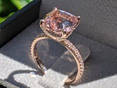 a fancy pink diamond ring sits in a box on the ground next to some flowers