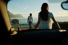 a man and woman standing in front of a car looking out at the ocean