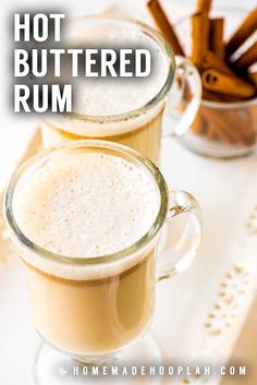 two mugs of hot buttered rum with cinnamon sticks in the background and text overlay