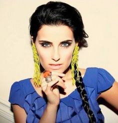 a woman with black hair and blue shirt holding a donut in her hand while wearing large yellow earrings