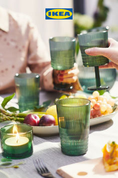 people are sitting at a table with green glasses and plates full of food in front of them