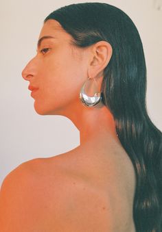 a woman with long black hair wearing large silver hoop earrings on her back, looking off to the side