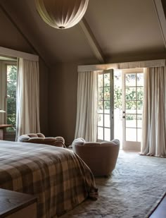 a large bed sitting in a bedroom next to two chairs and a window with curtains