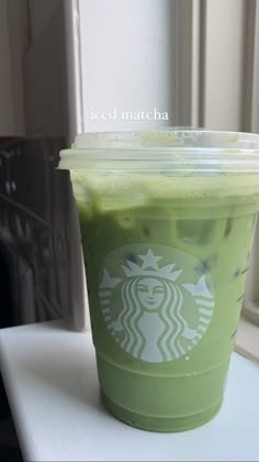 a green drink in a plastic cup sitting on top of a counter next to a window