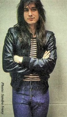 a woman standing with her arms crossed in front of a wall wearing blue jeans and a black leather jacket