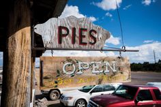 a wooden sign that says pies on the side of a building next to parked cars