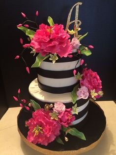 a black and white striped cake with pink flowers on the top tier is decorated with gold glitter