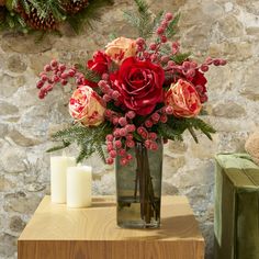 a vase filled with red and pink flowers on top of a table next to two candles