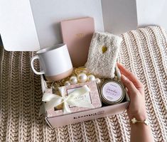 a woman's hand is holding a gift box with pearls, soap and other items