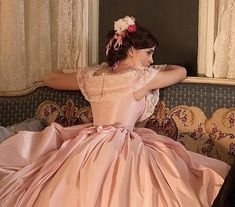 a woman sitting on top of a couch wearing a pink dress and flower in her hair