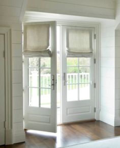 the inside of a house with white walls and wooden floors, two french doors leading to an outside deck