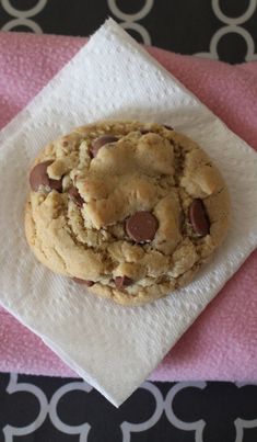 a chocolate chip cookie sitting on top of a white napkin next to a pink towel