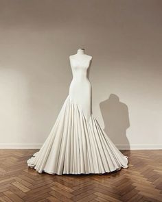 a mannequin is standing in front of a white dress on a wooden floor