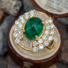 This elegant ring is centered with an oval, emerald cabochon in a four-prong setting. The center is accented with twenty-six (26) prong set, round brilliant cut diamonds and eight (8) channel set, baguette cut diamonds. The ring measures 21.3mm at the top, rises 13.9mm above the finger, tapering to 2.8mm wide and 0.8mm thick at the base of the shank. Currently size 9.5. Antique Cocktail Ring, Antique Engagement Rings Sapphire, Ballerina Ring, Colombian Emerald Ring, Estate Jewelry Rings, Emerald Cabochon, Wedding Ring Diamond Band, Baguette Cut Diamond, Antique Engagement Rings