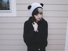 a young woman wearing a panda hat and black sweater standing in front of a house