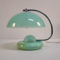 a green lamp sitting on top of a table next to a white wall and floor