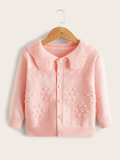 a pink cardigan sweater hanging on a wooden hanger with an embroidered flower design