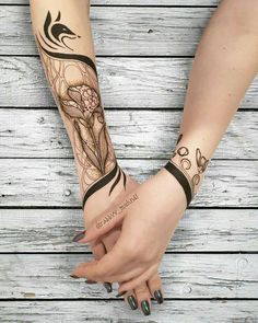 two hands holding each other with tattoos on their arm and wrist, one has a flower in the middle