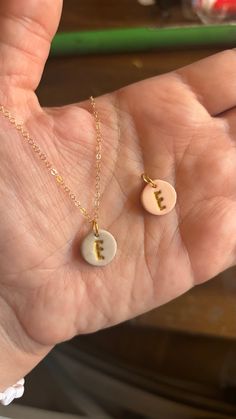 a person's hand holding two necklaces with letters on them