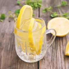 a glass mug filled with lemonade on top of a wooden table next to sliced lemons