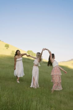 three women in dresses are standing in the grass and holding their hands up to each other