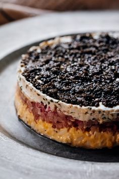 a cake sitting on top of a white plate covered in black and red toppings