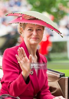 a woman in a pink suit and hat sitting on a bench with her hand up