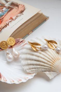 two pearl earrings sitting on top of a shell next to a book and seashell