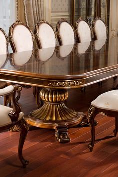 a dining room table with white chairs and gold trim around the edges, in front of a mirror