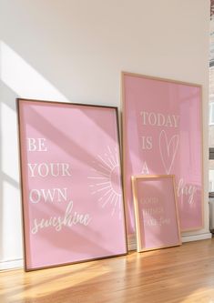 two pink posters on the wall in an empty room with sunlight coming through them, and one is saying be your own sunshine