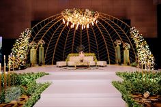 a stage set up for a wedding ceremony with flowers and greenery on the floor