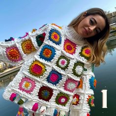 a woman is holding up a crocheted granny's afghan by the water