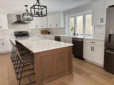 a kitchen with white cabinets and marble counter tops, an island in the middle is surrounded by barstools