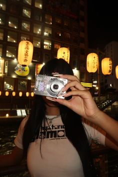 a woman holding up a camera to take a photo in front of chinese lanterns at night