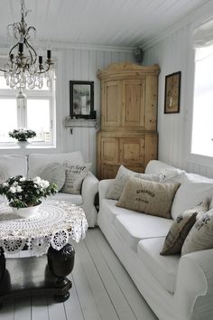 a living room filled with white furniture and a chandelier hanging from the ceiling