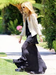 the blonde woman is walking down the sidewalk in her long black dress and white jacket