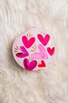 a pink heart shaped case sitting on top of a white fur covered surface with hearts painted on it