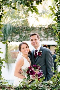 a bride and groom pose for a photo in front of greenery at their wedding