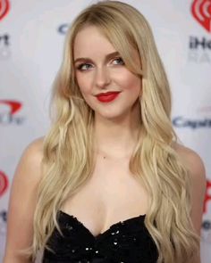 a woman with long blonde hair and red lipstick wearing a black dress at an event