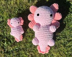 two pink crocheted elephants laying in the grass with one holding its baby's head