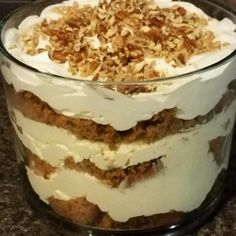 a layered cake with white frosting and toppings in a glass dish on a granite countertop