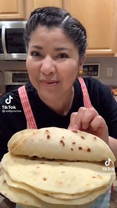 a woman in an apron is holding a stack of tortillas