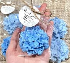 a person holding a blue flower in their hand with some tags on the top of it