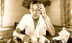 a man sitting at a table with a pen and paper in front of his face