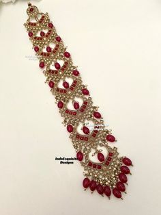 a bracelet with red stones and pearls on it's side, sitting on a white surface