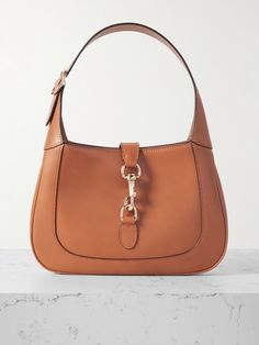 Gucci's small 'Jackie' bag takes its curved silhouette from the original style that debuted in the '60s and even boasts the same gold-tone piston clasp. Crafted in Italy from brown leather, it's suspended on a thick strap that can be adjusted to your perfect drop. It has plenty of space inside for everyday essentials, like your wallet, keys, cell and compact. Gucci Leather Bags With Brass Hardware, Gucci Shoulder Bag With Brass Hardware For Evening, Gucci Shoulder Bag With Brass Hardware For Formal Occasions, Classic Gucci Shoulder Bag With Palladium Hardware, Gucci Leather Shoulder Bag With Brass Hardware, Gucci Formal Shoulder Bag With Brass Hardware, Elegant Shoulder Bag With Horsebit Detail For Work, Timeless Office Bag With Horsebit Detail, Classic Gucci Shoulder Bag With Metal Hardware