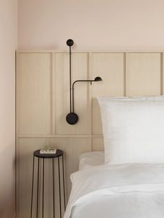 a bed with white sheets and pillows next to a wall mounted coat hook on the headboard