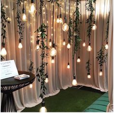 the lights are hanging down from the ceiling in front of the curtained room with white drapes and greenery