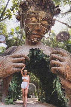 a woman is standing in front of a statue that looks like a human face with hands on her head