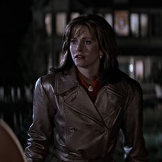 a woman wearing a brown leather jacket and red shirt standing in front of a house at night